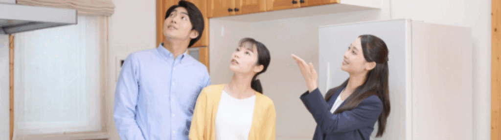 内覧中のキッチンで天井を見上げる若い夫婦と説明する女性スタッフ