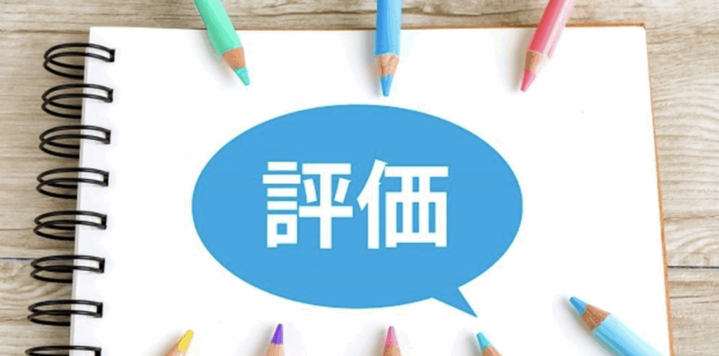 評価をイメージした写真—ノート中央の吹き出しに「評価」の文字、周囲にカラフルな色鉛筆が並ぶ